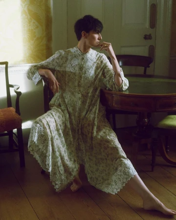 Short-haired woman in a patterned long-sleeved dress seated indoors near a wooden table