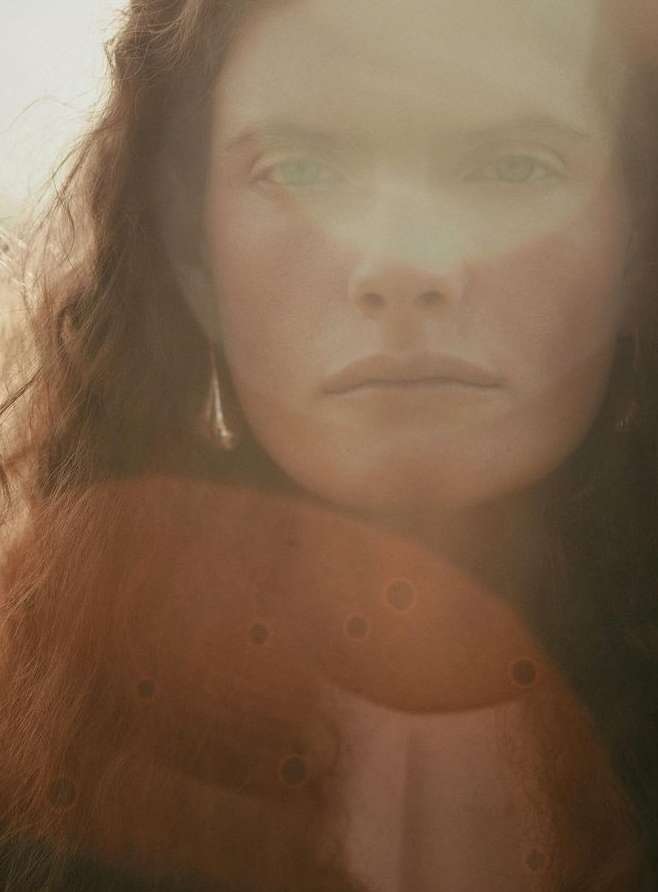 Close-up portrait of a woman with curly red hair and light skin, featuring a diffused light effect, creating an ethereal and soft focus.