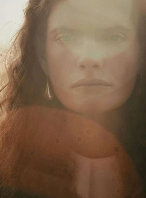 Close-up portrait of a woman with curly red hair and light skin, featuring a diffused light effect, creating an ethereal and soft focus.