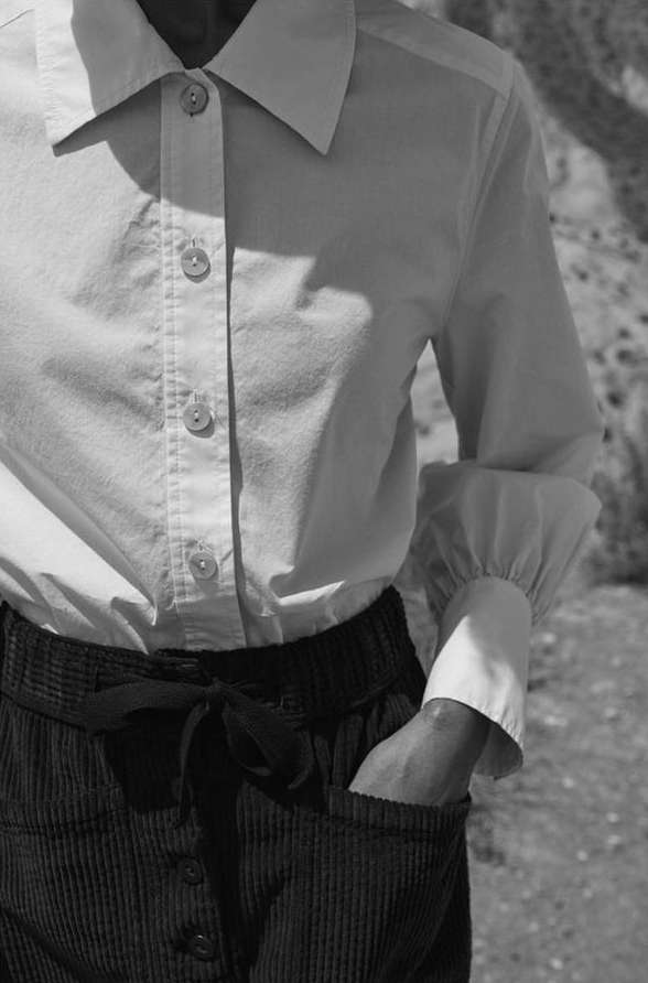 Close-up studio shot of a person wearing a button-down shirt and corduroy pants with a drawstring, featuring muted black and white tones.