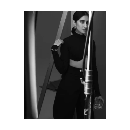 Black and white portrait of a woman in a black mock neck top holding a glass near studio equipment in London by Agata Pospieszynska