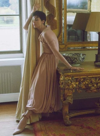 Woman with short dark hair in a pink dress posing beside a window and a gilded console table, captured by Agata Pospieszynska.