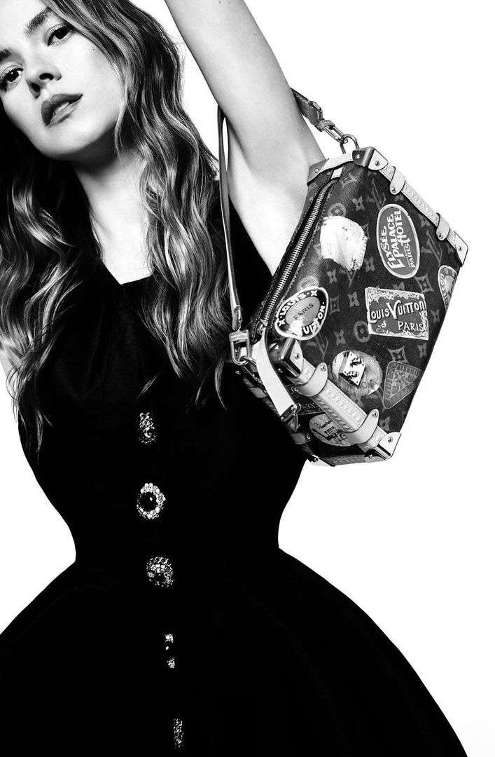 Model in black dress lifting a monogram handbag with travel stickers, photographed by Agata Pospieszynska