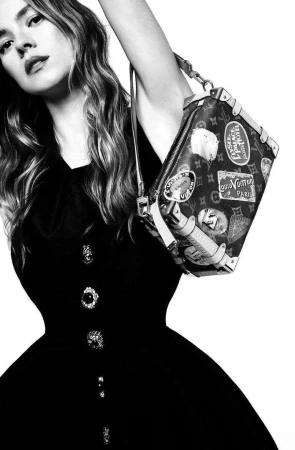 Model in black dress lifting a monogram handbag with travel stickers, photographed by Agata Pospieszynska