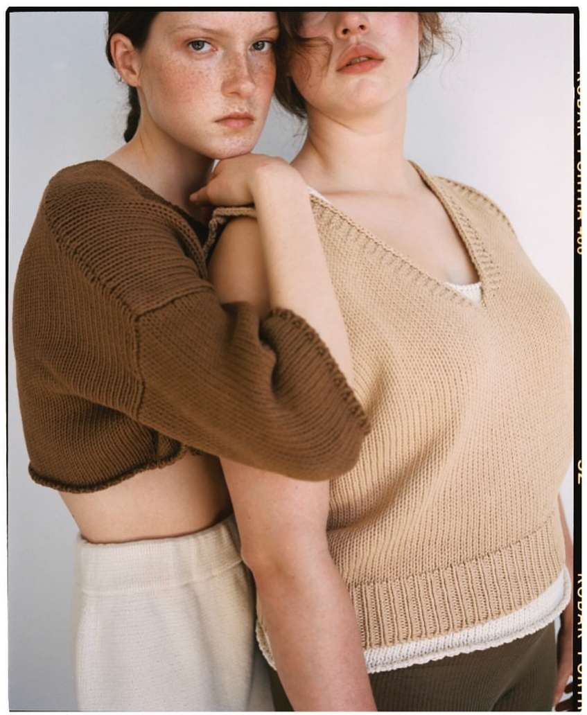 Two fair-skinned young women pose in knit tops and neutral pants against a plain background, with film border and soft lighting.