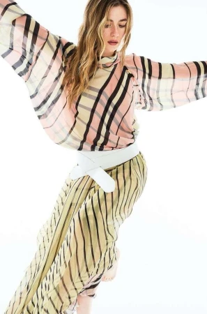 A woman poses in a pink and yellow striped dress with a white belt against a white backdrop, creating a light, airy fashion image.