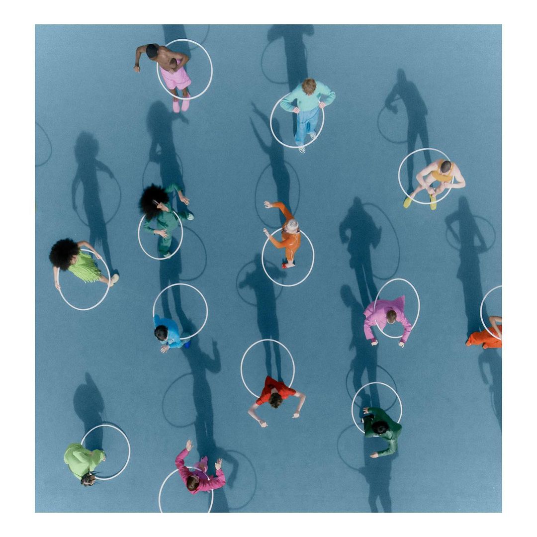 Overhead shot of diverse people in colorful clothing standing inside white circles on a blue surface with shadow casting.