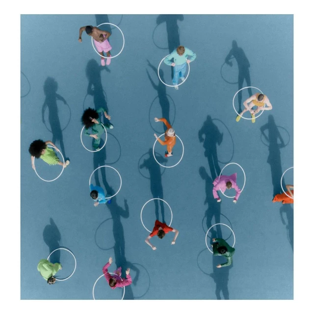 Overhead shot of diverse people in colorful clothing standing inside white circles on a blue surface with shadow casting.