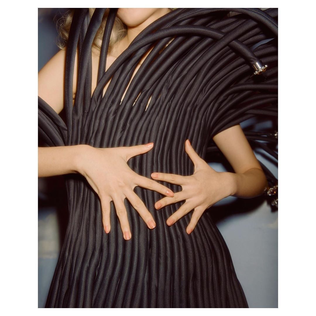 Fashion shot of a person posing in an avant-garde black dress with hands raised, soft studio lighting, medium shot, artistic clothing design.