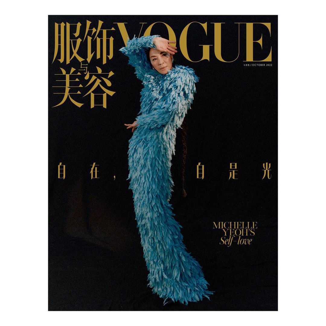 Michelle Yeoh on Vogue cover in blue feathered dress. Magazine cover features gold Vogue logo and various text elements on black.