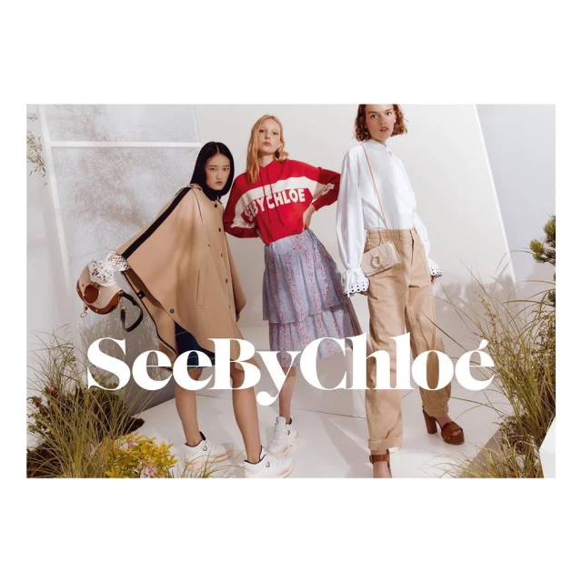 Three women model See By Chloé apparel in a studio. An Asian woman wears a cape with a purse; the other two wear casual outfits.
