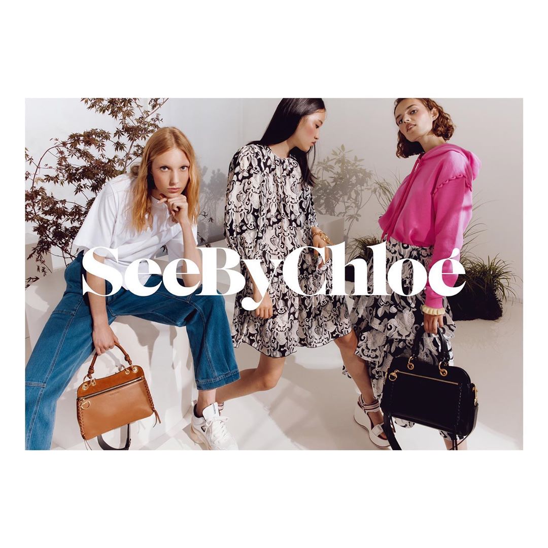 Three fashion models showcase See By Chloé handbags. The women pose indoors, styled in dresses, jeans, and a hoodie, complemented by purses.