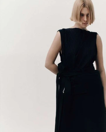 Model with short blonde hair wearing a dark sleeveless top against a plain white background