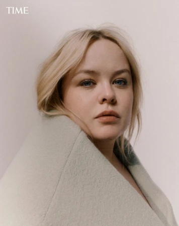 Portrait of a blonde woman wrapped in a light sage green coat against a neutral background with TIME logo