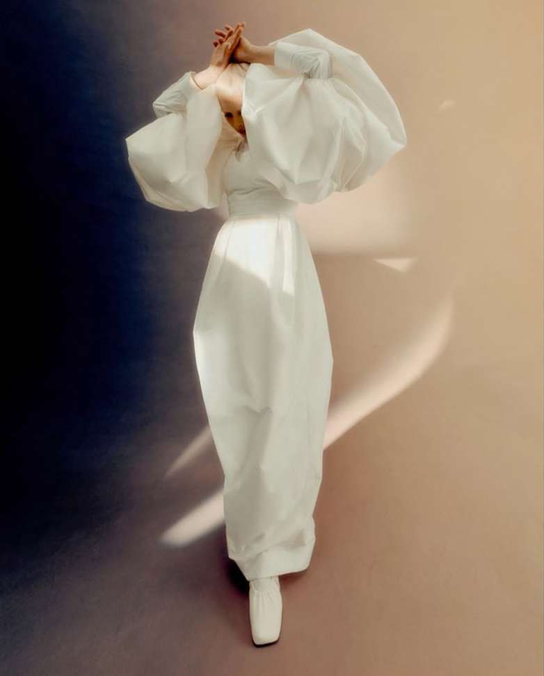 Fashionable woman posing in a puffy-sleeved white dress on a contrasting background of dark blue and light peach, studio lighting.