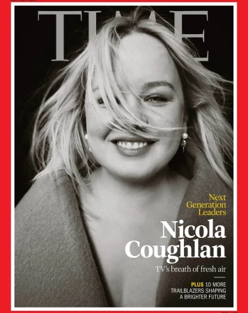 Close-up magazine cover portrait of Nicola Coughlan smiling with blonde hair blowing across her face against a dark background.