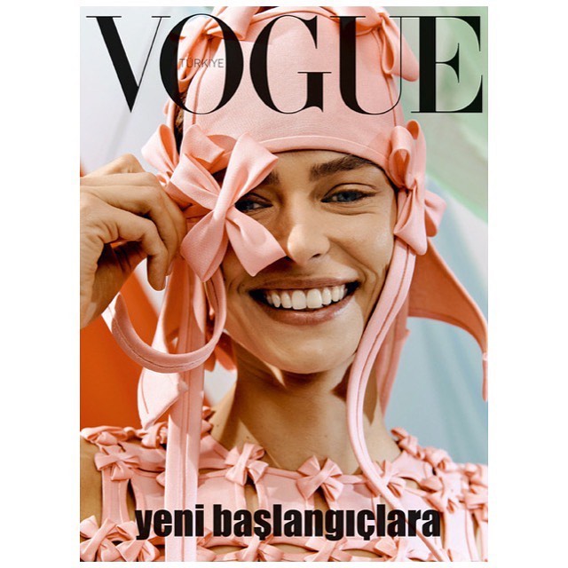 Vogue Turkey magazine cover featuring a smiling woman with fair skin and blue eyes wearing a light pink dress and hat with bow details.