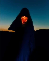 Silhouette of a veiled person standing against a twilight sky with a bright orange neon light illuminating their face