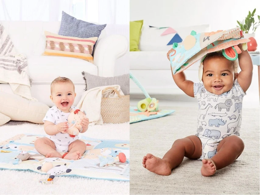 Two adorable babies, one holding a chicken toy while sitting on a play mat in front of a couch and the other holding a book.