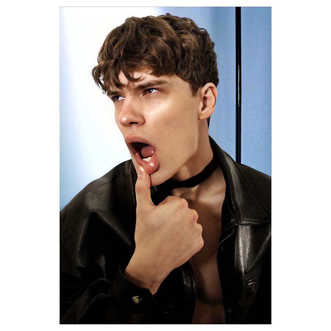 Close-up portrait of a young man with curly brown hair wearing a black leather jacket and choker by photographer Ahmed Hassan.
