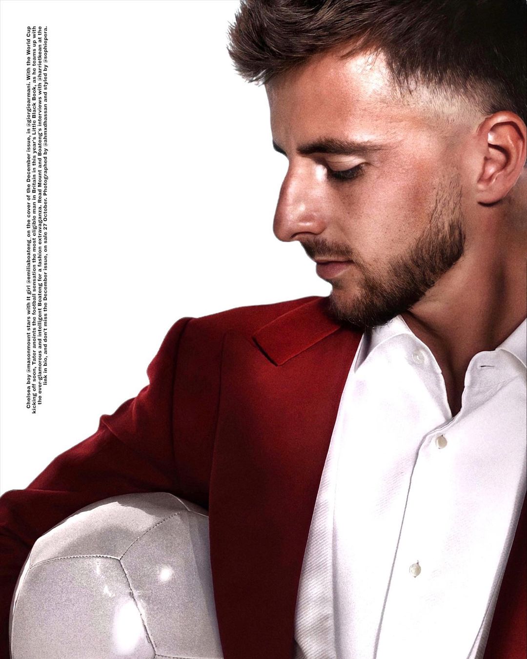 Portrait of a male model in a red suit and white shirt holding a soccer ball, shot in a photo studio with bright lighting.