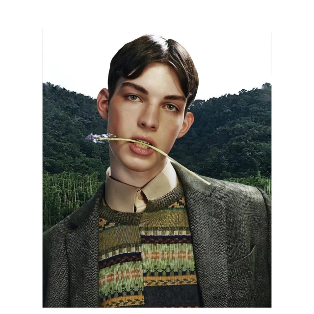Portrait of a young adult male with dark hair, wearing a tweed jacket and patterned sweater, holding a purple flower in his mouth outdoors.