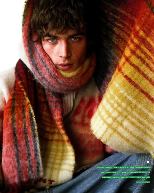 Close-up of a fair-skinned adult male wearing a multi-colored plaid scarf wrapped around his head and neck, gazing at the camera.