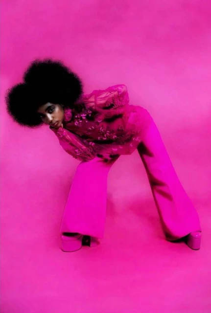 Fashion editorial shot of a woman with afro wearing pink top and pants on a pink seamless background in a bent over pose.