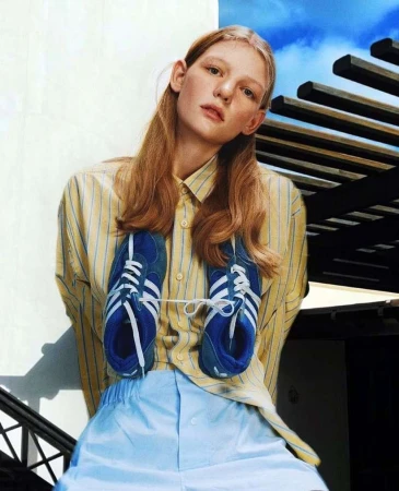 Model in a yellow striped shirt and light blue trousers holding blue sneakers against their chest by Ahmed Hassan