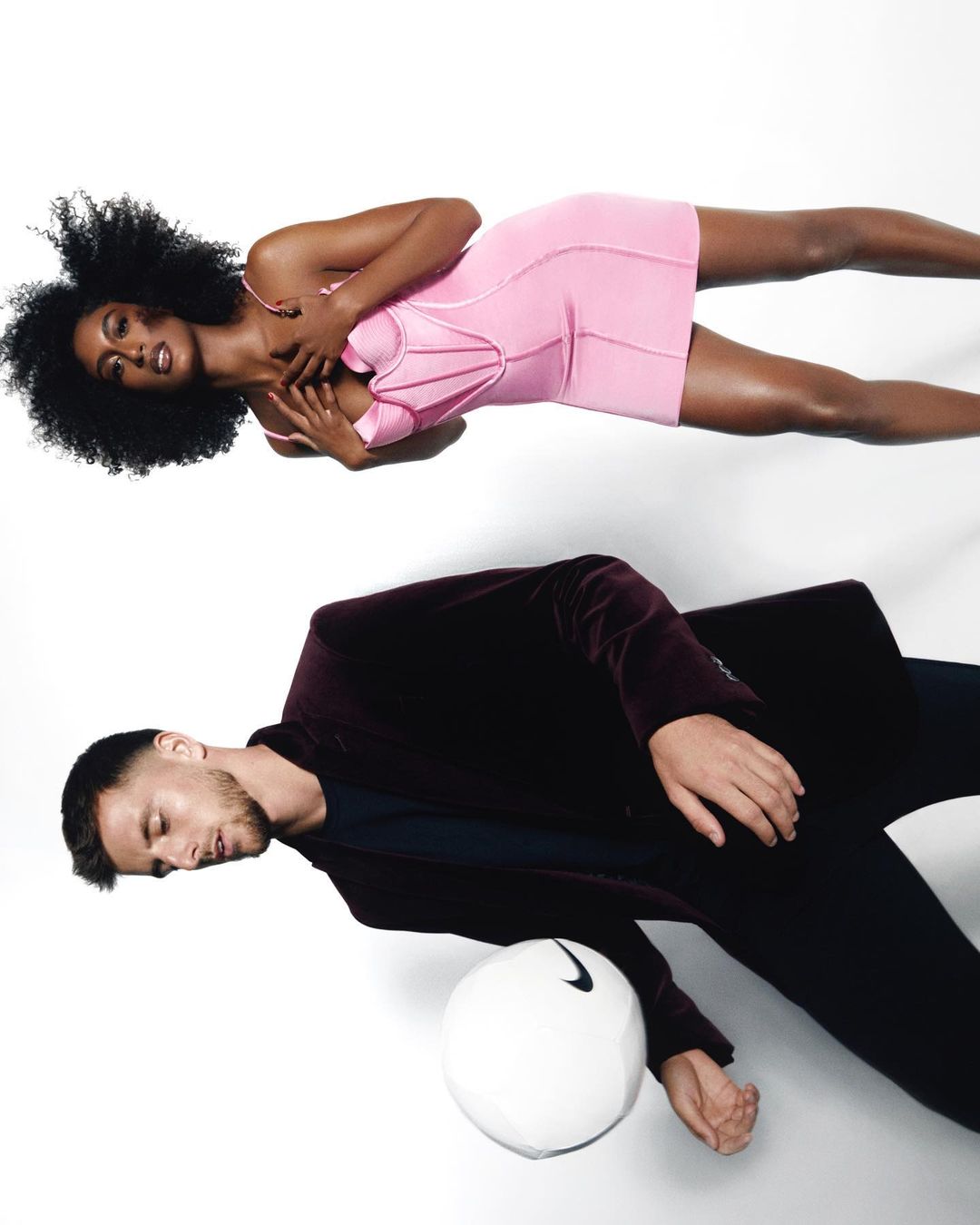 Fashionable athletic theme with Black woman in pink mini-dress, and Caucasian man in a burgundy velvet jacket and Nike soccer ball.