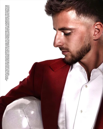 Close-up profile portrait of a man in a red blazer and white shirt holding a shiny silver football.