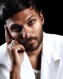 Close-up portrait of a man in a white blazer resting his chin on his hand against a black background