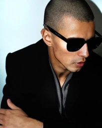Close-up portrait of a man wearing dark sunglasses and a black coat against a light background by Ahmed Hassan