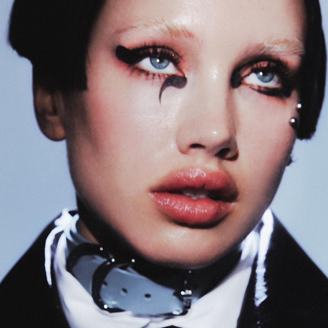 Close-up portrait of a woman with dramatic black eyeliner and a white collar, with focus on beauty, makeup, and fashion.