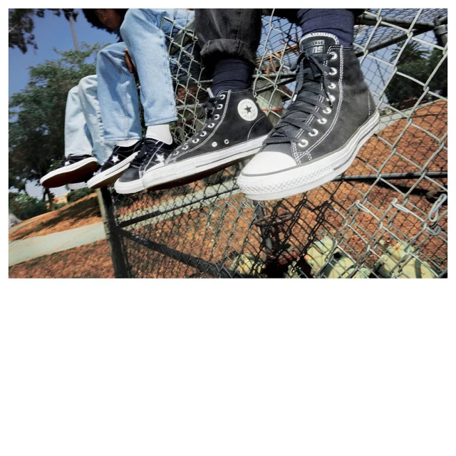 Three pairs of black and white Converse sneakers on a metal fence, showcasing high-top and low-top styles with blue skies and trees in the background.