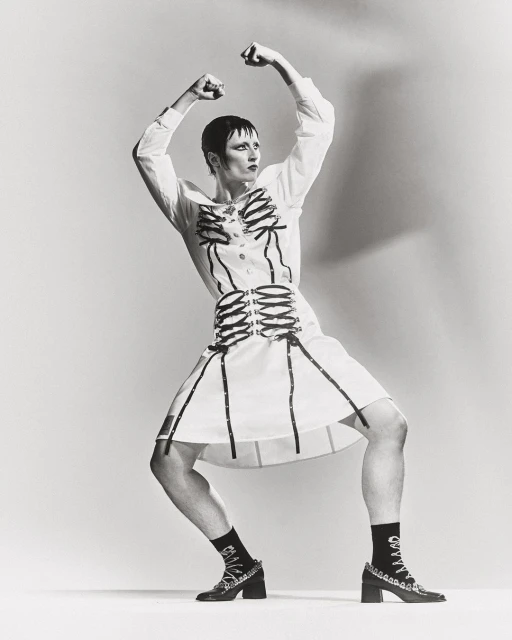 Person in white dress with black skeleton design, black socks and heels, posing against a white background in a studio.