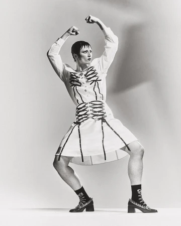 Person in white dress with black skeleton design, black socks and heels, posing against a white background in a studio.