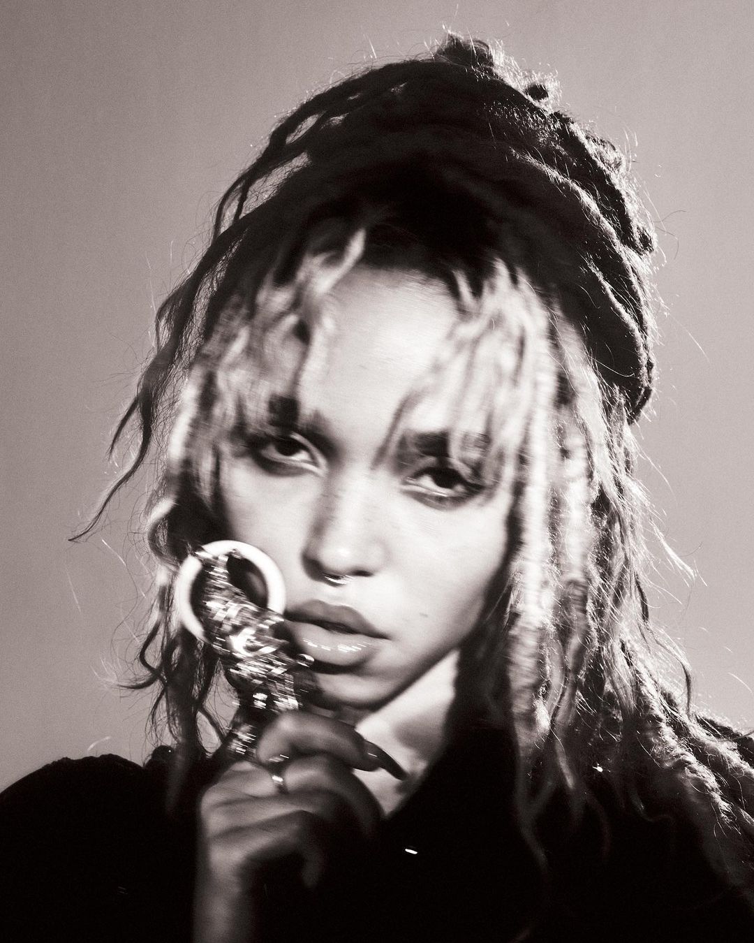 Monochrome portrait of a young adult woman with dreadlocks holding an ornamental ring, showcasing a fine-art beauty aesthetic.