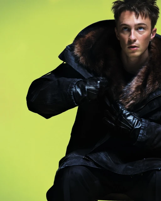 Stylish man in a fur-lined coat posing against a vibrant chartreuse background, showcasing a blend of fashion and editorial.