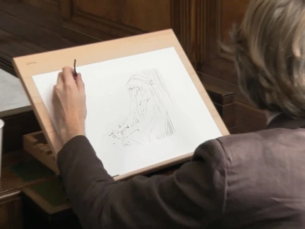 Artist working on a drawing of a person in an indoor setting, utilizing a thin brush to create details on white paper.