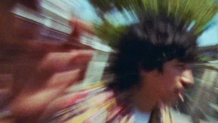 Motion-blurred photographic still by Aidan Zamiri featuring a person with dark hair and a patterned shirt
