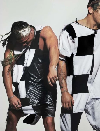 Two men wearing black and white checkered outfits standing against a plain white background by photographer Aidan Zamiri.