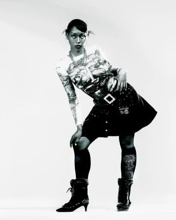 Black and white portrait of a woman posing in a patterned top and dark skirt against a plain studio background.