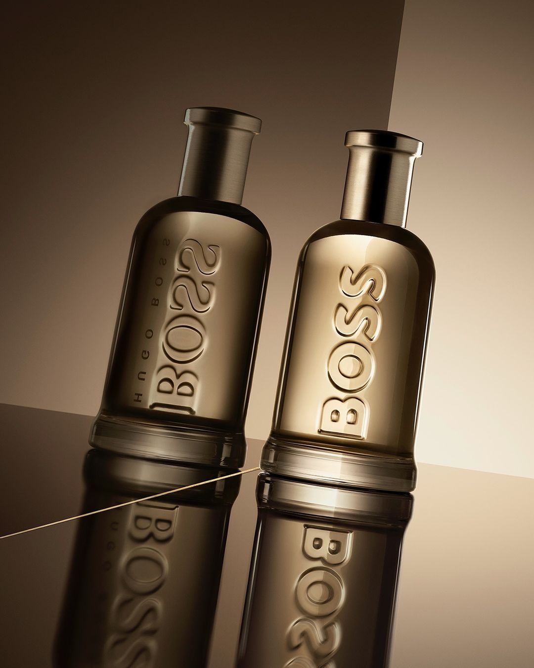 Two Hugo Boss perfume bottles are displayed close-up with reflective surfaces and studio lighting, creating a luxurious, elegant product shot.