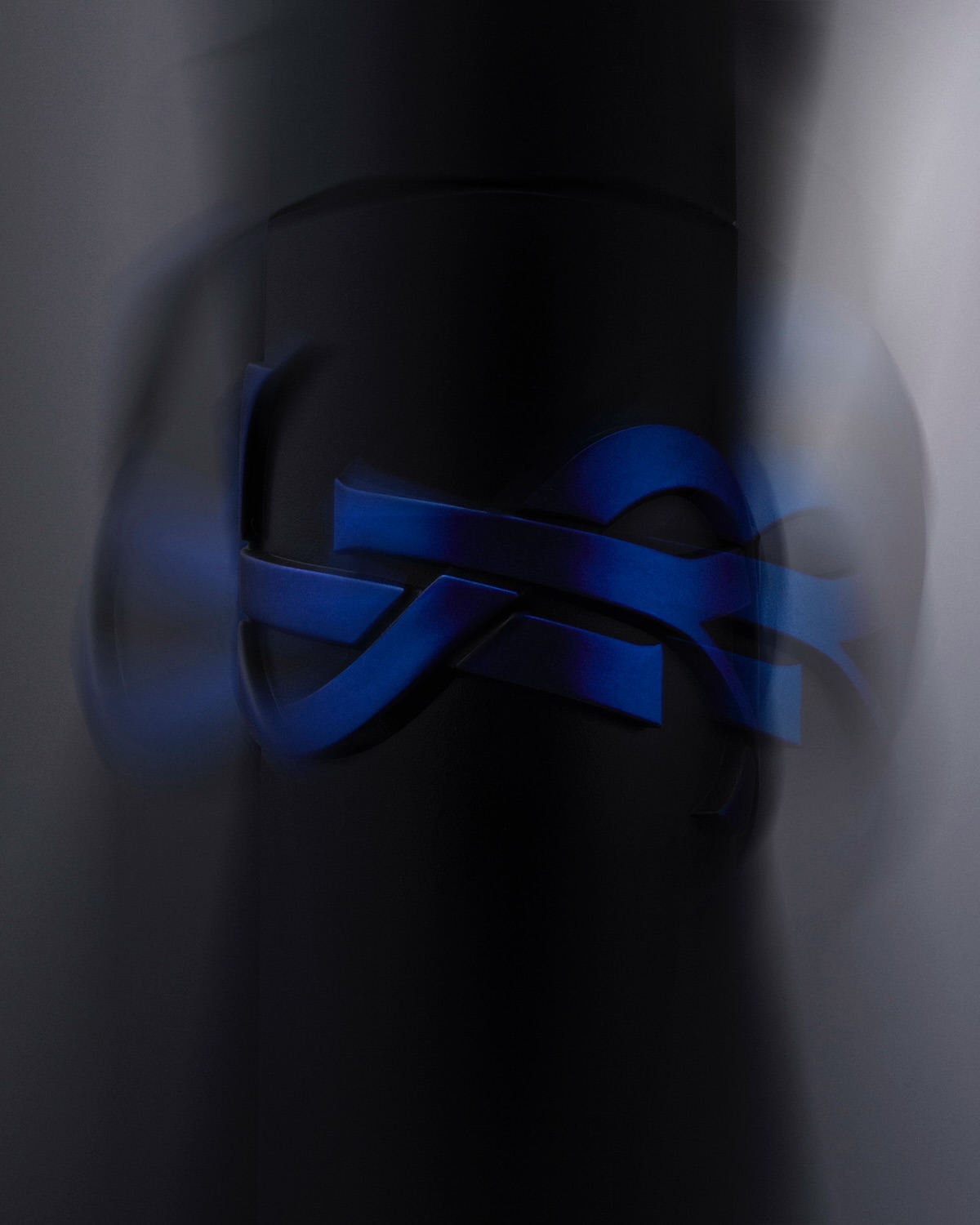 Abstract macro photography of a curved, geometric blue logo on a dark grey background, soft focus, and shallow depth of field.