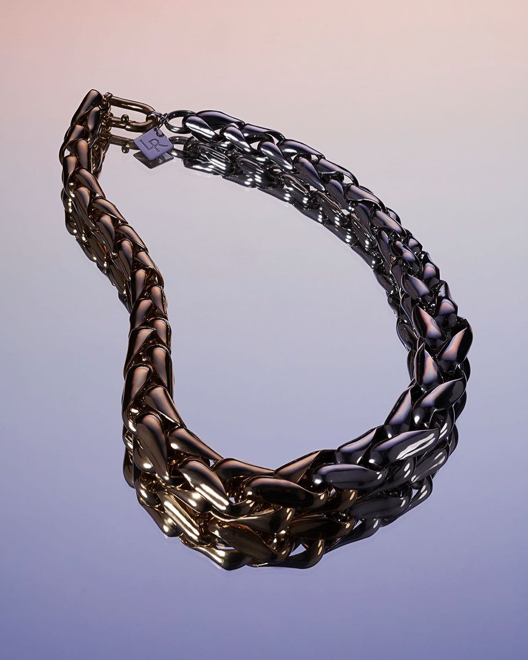 Close-up of a gold and silver chain necklace in a studio setting against a gradient purple background, showcasing high-end jewelry.