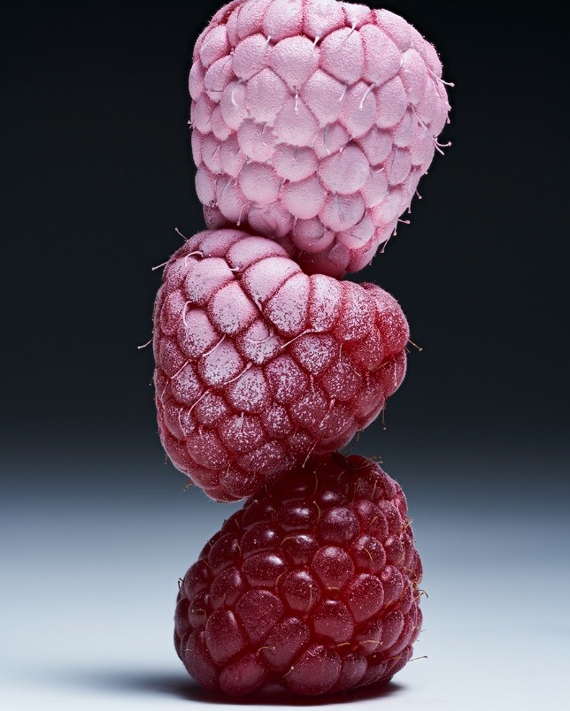 Stack of three raspberries showing gradient of pink, red and dark red on a black background, product food photography.