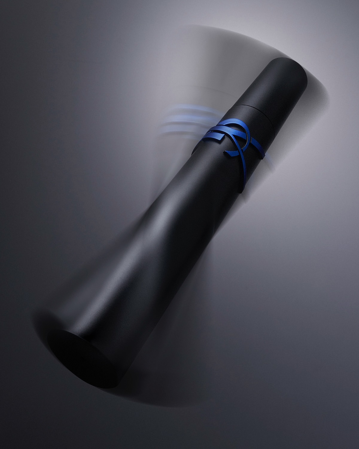 Black diploma tube with blue ribbon on gray background. Graduation or achievement concept in studio lighting. Formal presentation.