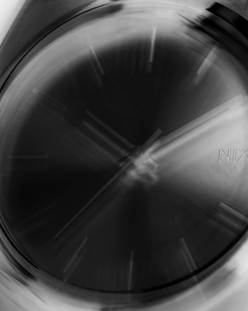 Close-up shot of a blurred silver wristwatch displaying the time with silver watch hands against a dark face and a silver case.