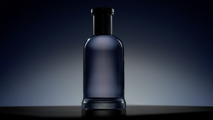 Elegant glass bottle with a black top on a reflective surface, set against a gradient blue background for a sophisticated product shot.